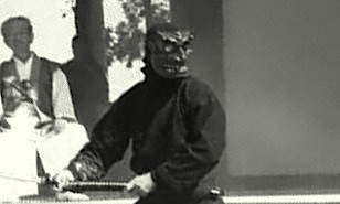 A member of the Bujinkan demonstrating kenjutsu in a demon mask whilst Soke Hatsumi witnesses